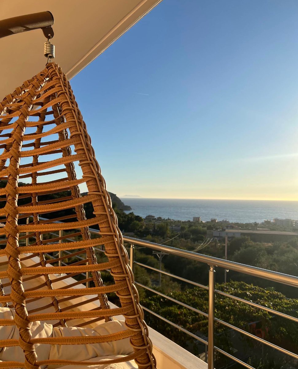 Balcony view from Apollon's Apartments in Himarë — hanging chair overlooking the Ionian Sea and Himarë bay at sunset